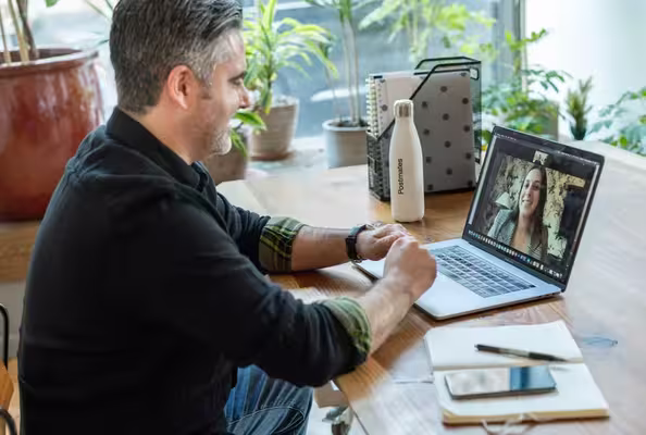 A man on a video call at a kitchen table.